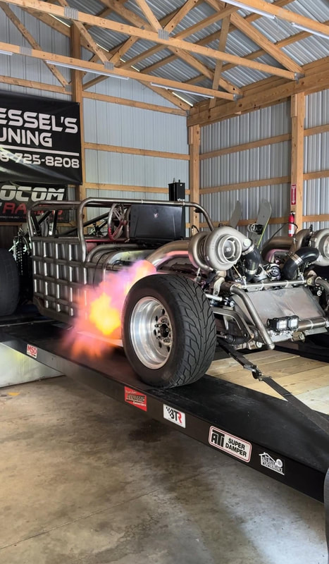 A bare metal twin turbo rail strapped down in the shop, flame off the header