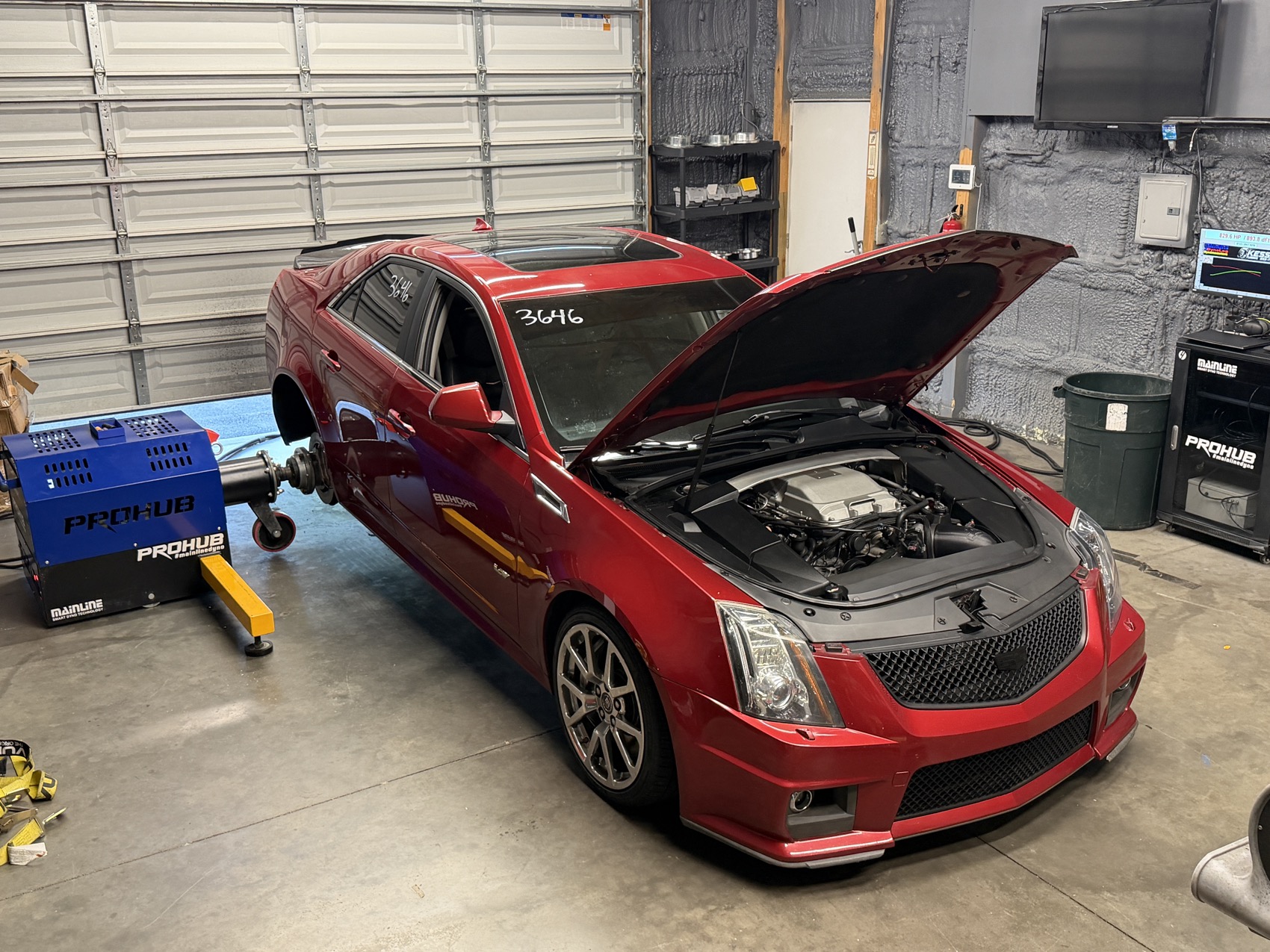 A red Cadillac CTS-V with the hood up on the dyno hubs in the shop