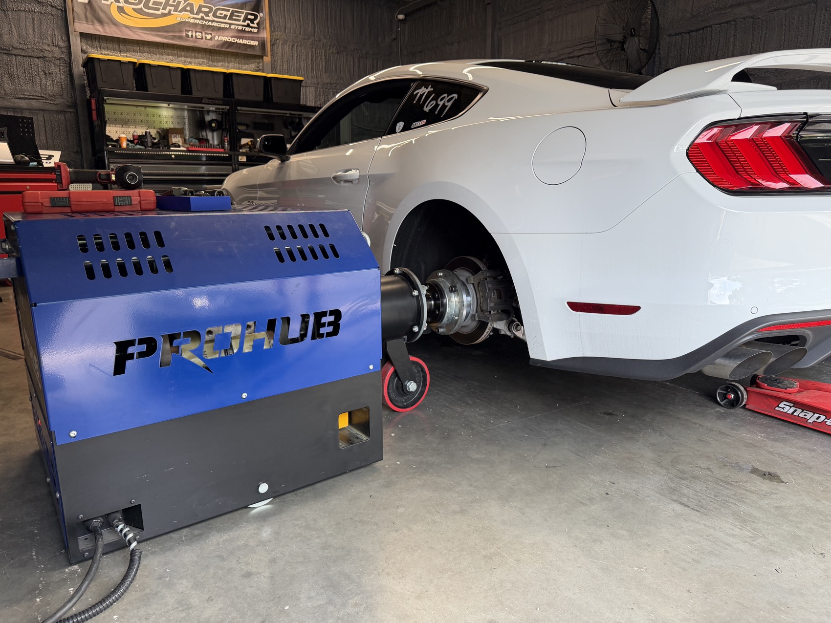A Mustang bolted to the dyno hubs in the shop bay